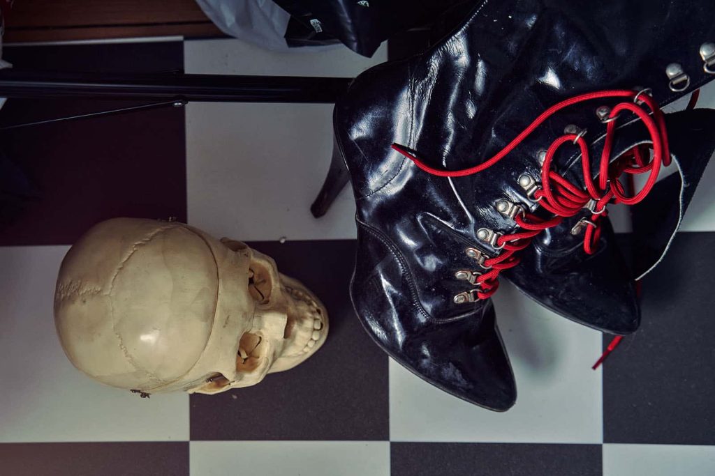 A Birdseye view of a checkered floor with a fake skull and a pair of shiny leather boot high heels with red laces