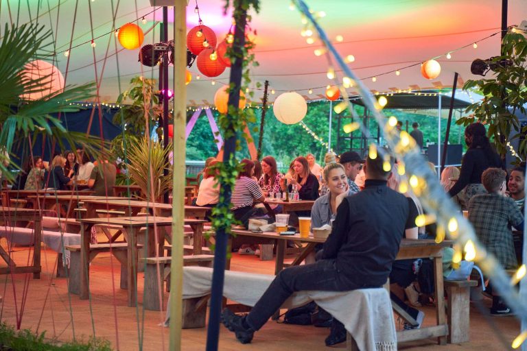 People sit in Mysabar, Norwich surrounded by fairy lights, hanging decorations.