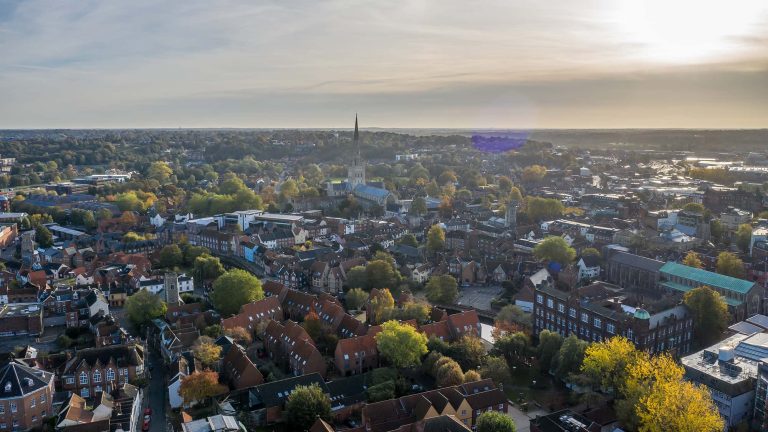 A cityscape of Norwich, overlooking trees, buildings, the Castle and the main Cathedral Spire