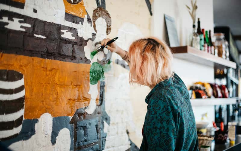 BA Fine Art student Elly Lynn painting a section of a mural for a wall inside a pub