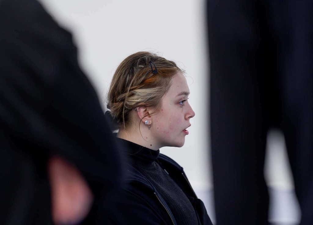 Side-profile of a student dressed all in black, through the blurred figures of other students, also wearing all black