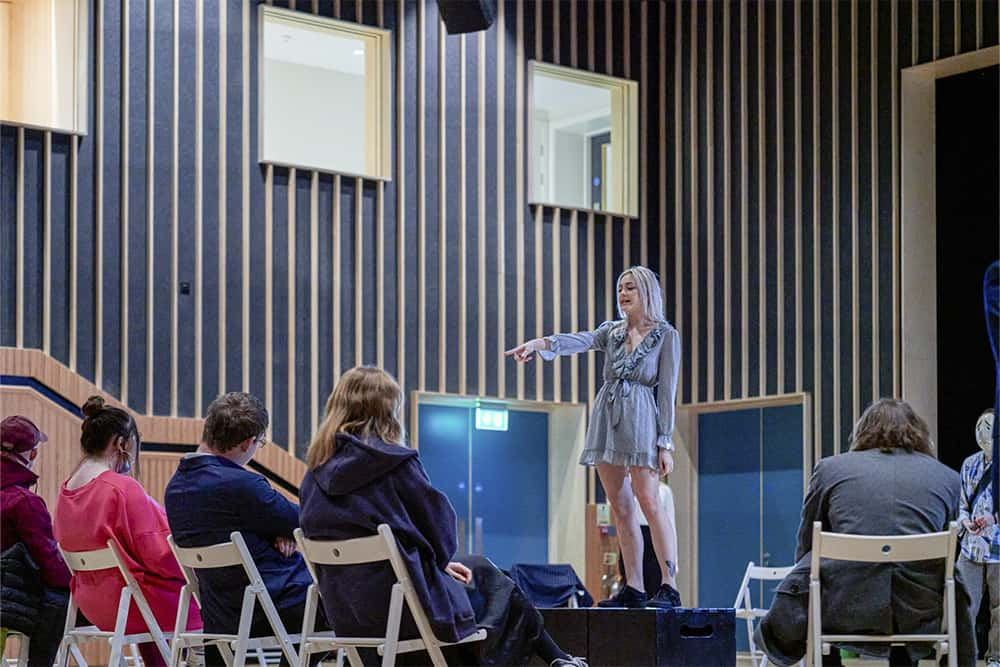 An acting student on stage pointing into a crowd