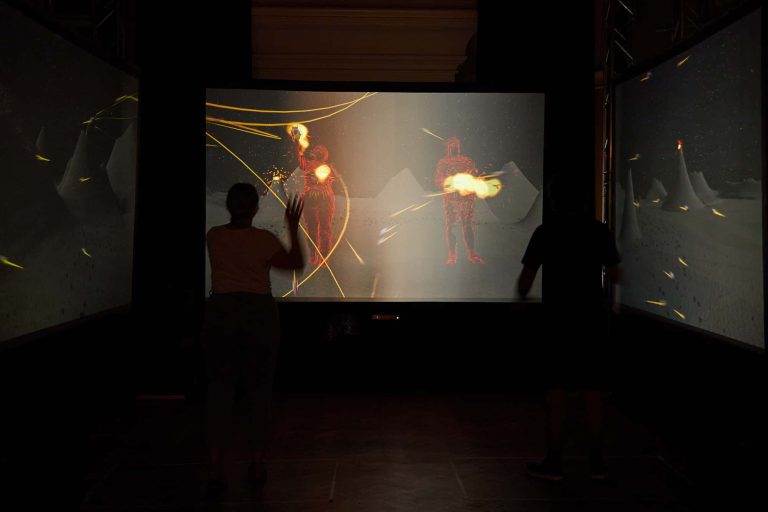 People attend The Multitude digital experience in a dark room, standing in front of a screen interacting with the artwork