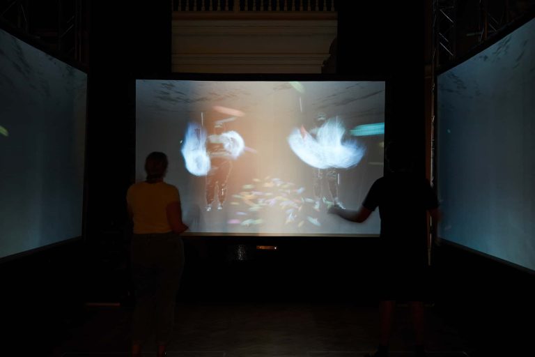 Two people stand in front of a digital artwork interacting with it