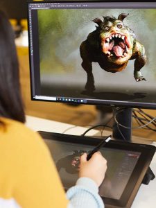 A student works using a graphics tablet and stylus to create detailed visuals of a 3D monster