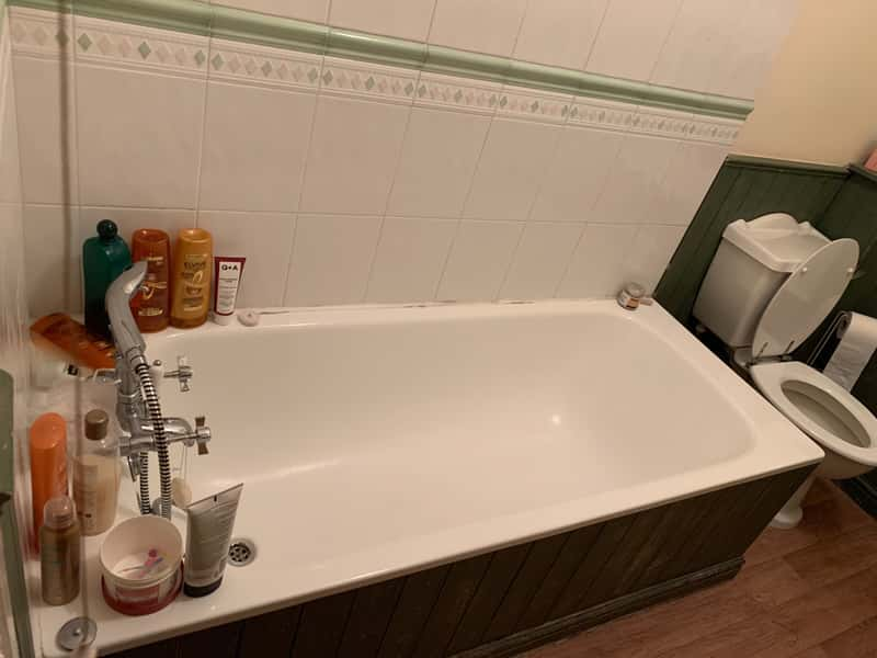 Photo of a bath in a shared bathroom in private student accommodation. Bottles of shampoo and bubble bath are placed by the taps