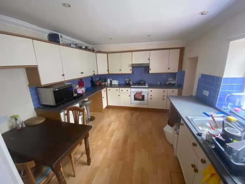 A shared kitchen in private student accommodation. Lots of cream and wood cabinets against a blue and cream wall, with a dark wood dining table