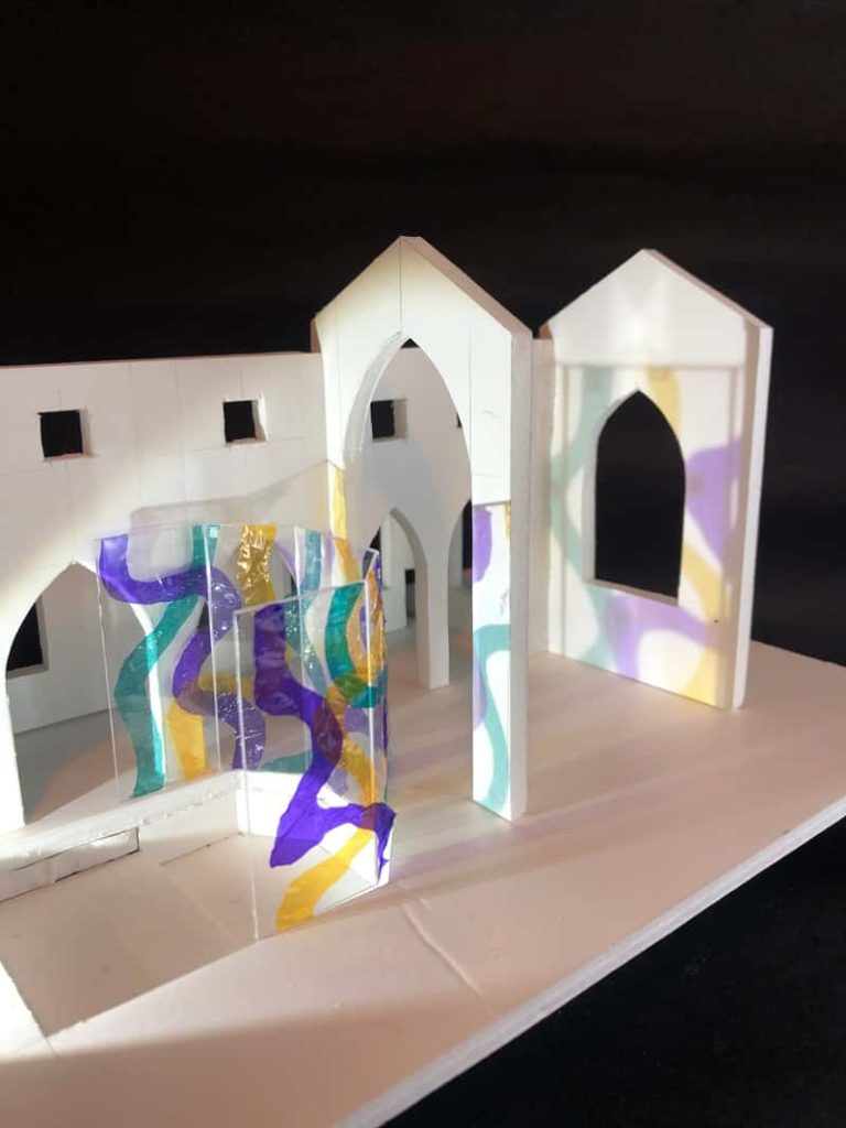 Minature 3D model of a church building which has a perspex wall with abstract colourful patterns. The patterns cast colourful shadows on the rest of the churches surfaces