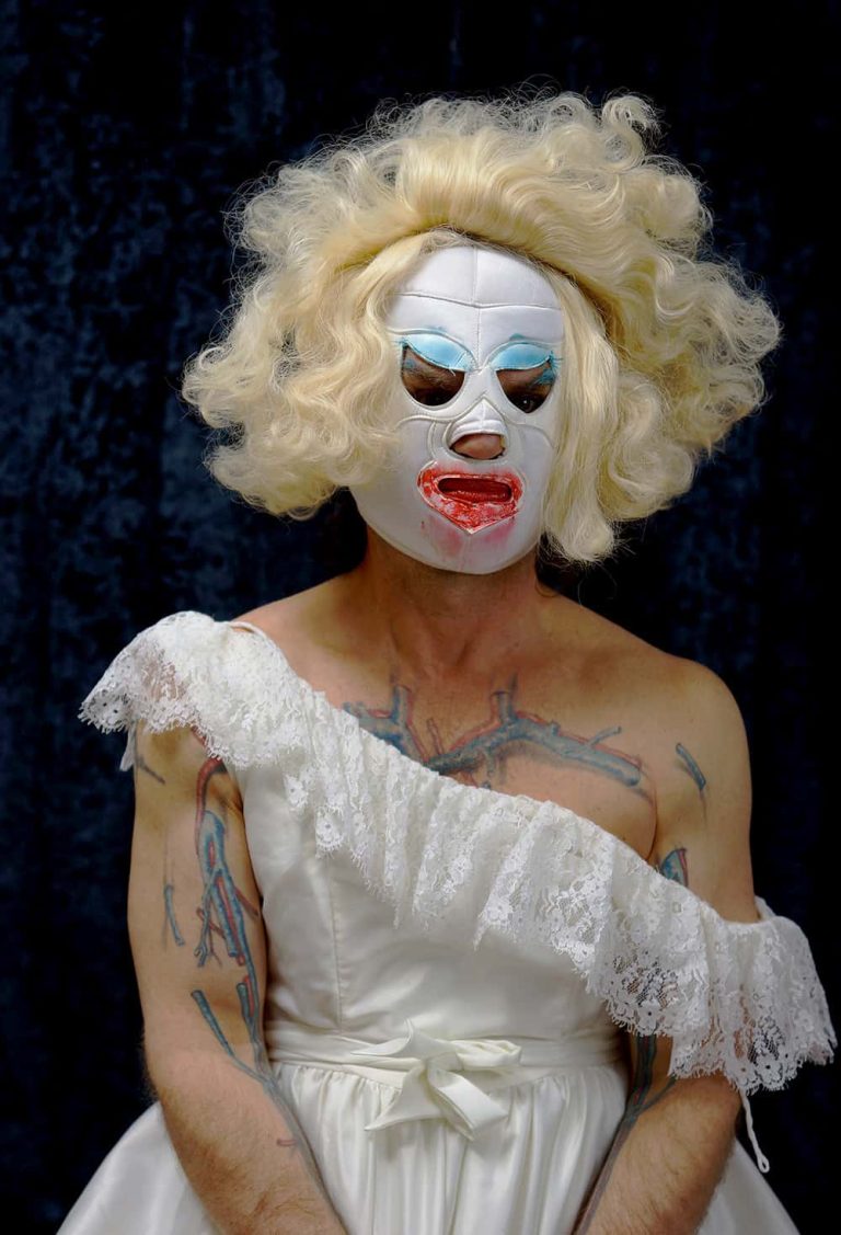 A person dressed up in a dress with tattoos on them, and a wig and a mask.