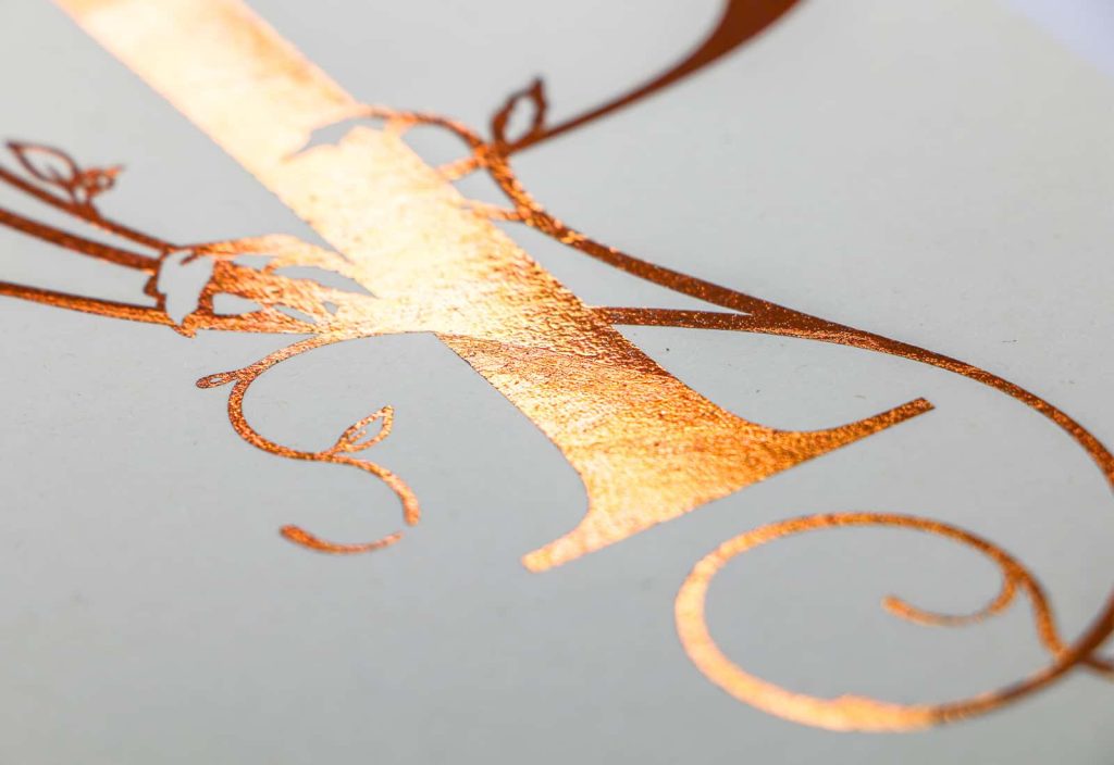 Close up image of student work making use of hot foil, to create a professional metallic finish. The image is the bottom of a serif letterform, with ornamental floral embellishments