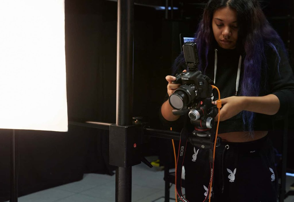 A photography student lines up a camera which is mounted on a sturdy metal pivot in the photography studio