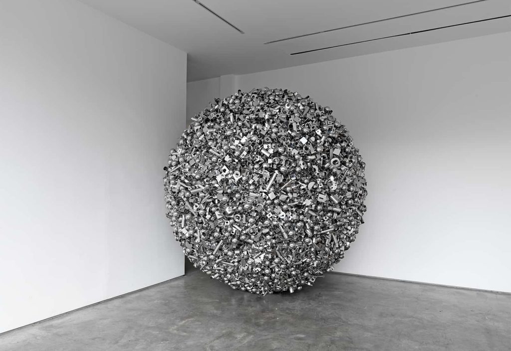 A large sphere made up of thousands of unidentifiable shiny stainless steel components of various sizes and shapes, the distribution of which has been decided using magnetic forces.