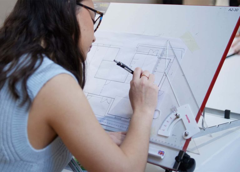 A student studying interior design at Norwich University of the Arts works calmly on a floor plan, using one of the drawing tables in the architecture and interior design studio space.