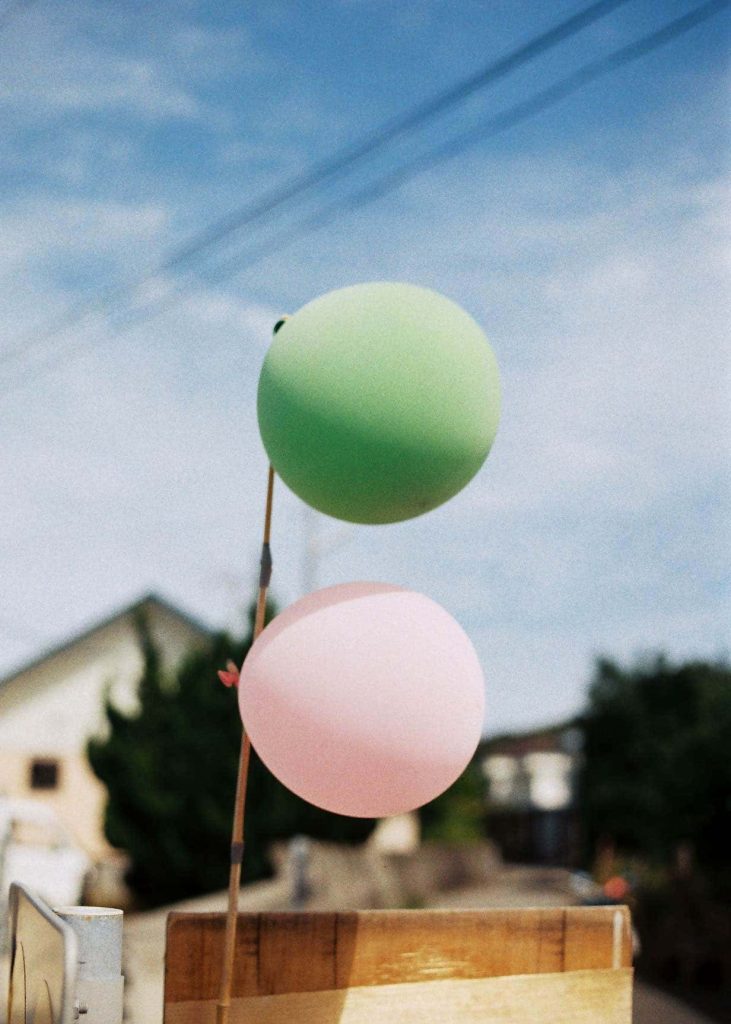 A green and pink balloon hanging from a pole, blowing in the wind