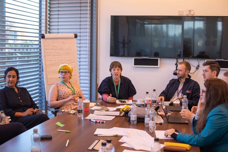 Six people sat in a room in front of two screens at a table at Norwich Research Park