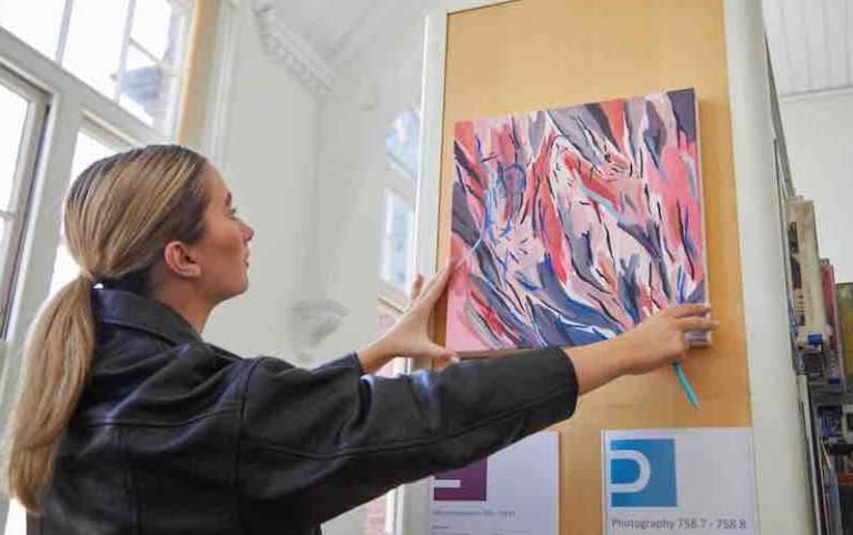 person placing abstract canvas painting onto side of library shelf holding books