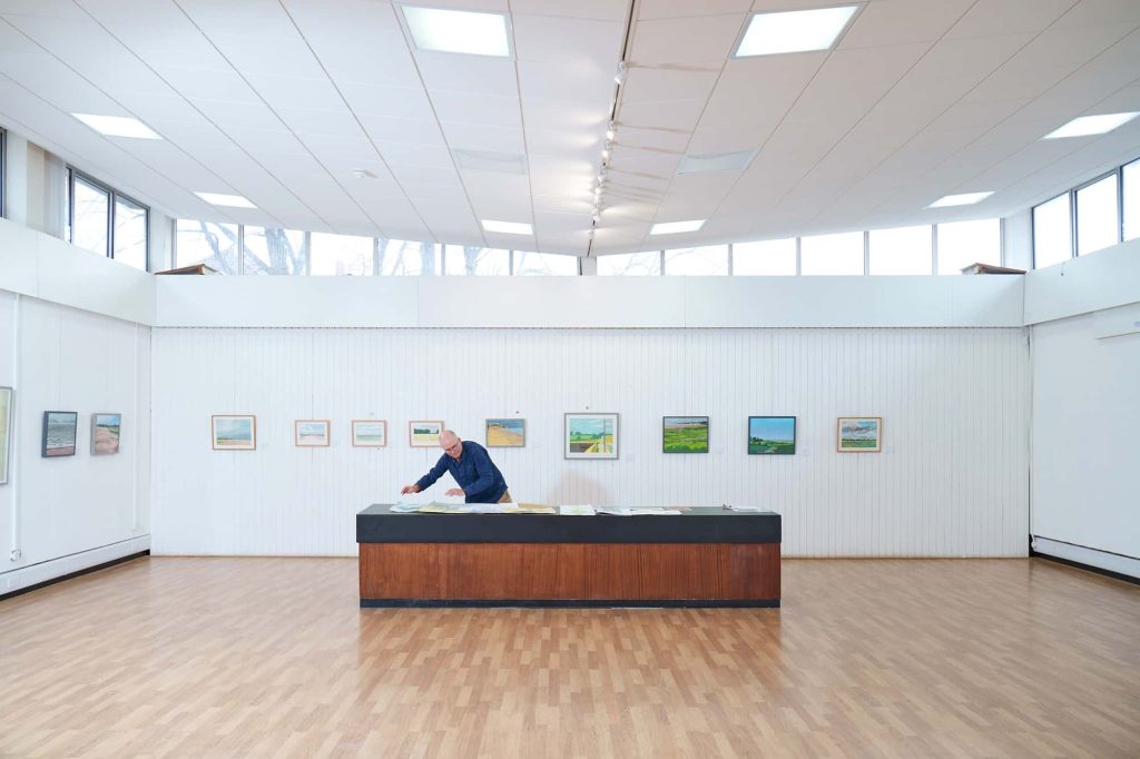 Will Jefferies looks at his artwork on a plinth in front of several of his paintings