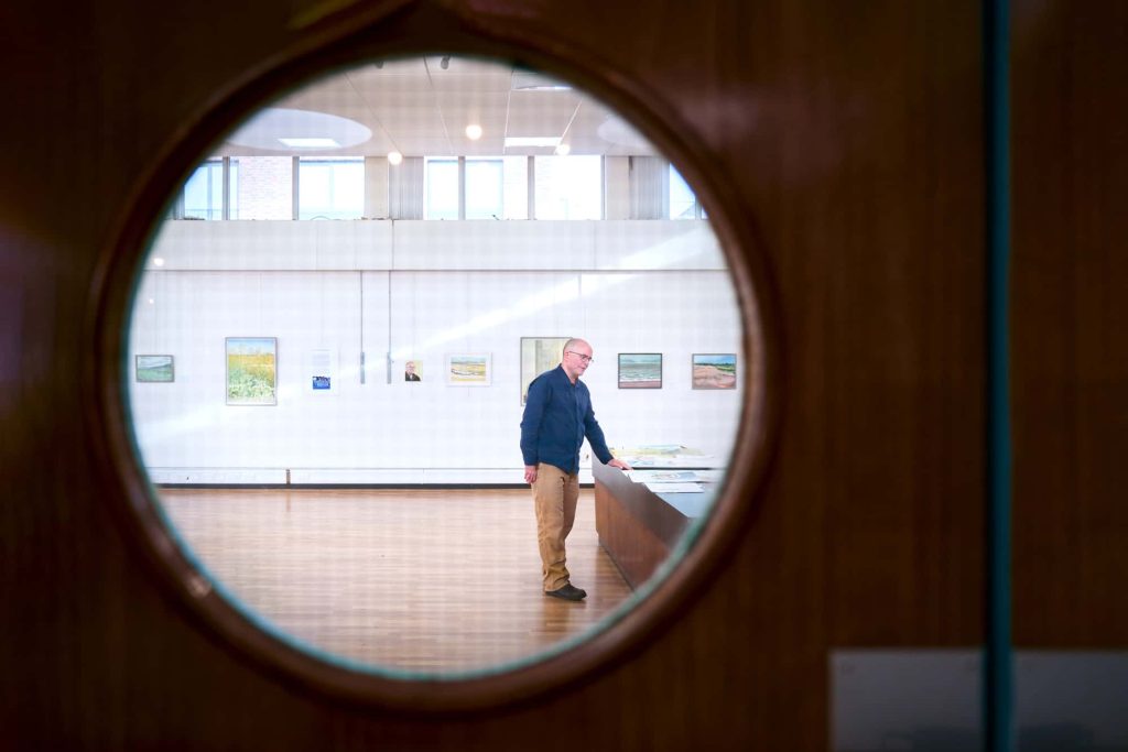 Will Jefferies through a door, looking at paintings, in front of exhibited art work