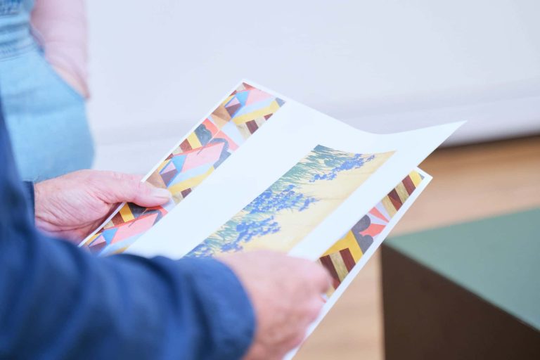 Will Jefferies holding several pieces of colourful artwork.