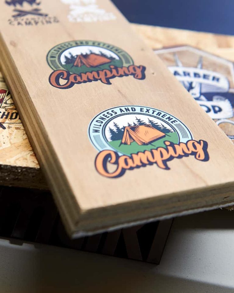 Pieces of rough wood, which have been printed on using the UV printer in the Norwich University of the Arts Digital Design Workshop. The printed image is a bold retro logo which has 'wildness and extreme' lettered on a circle, under 'camping' in orange lettering with a drop shadow. The centre of the circle is an old fashioned ridge style canvas tent.