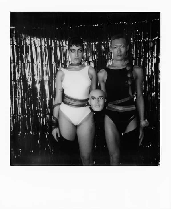 Original magazine editorial, two androgynous models in a dark room, shot on grainy and black and grey film. They are each wearing a cotton body, one white and one black, and each have a single leg covered, on opposite sides.