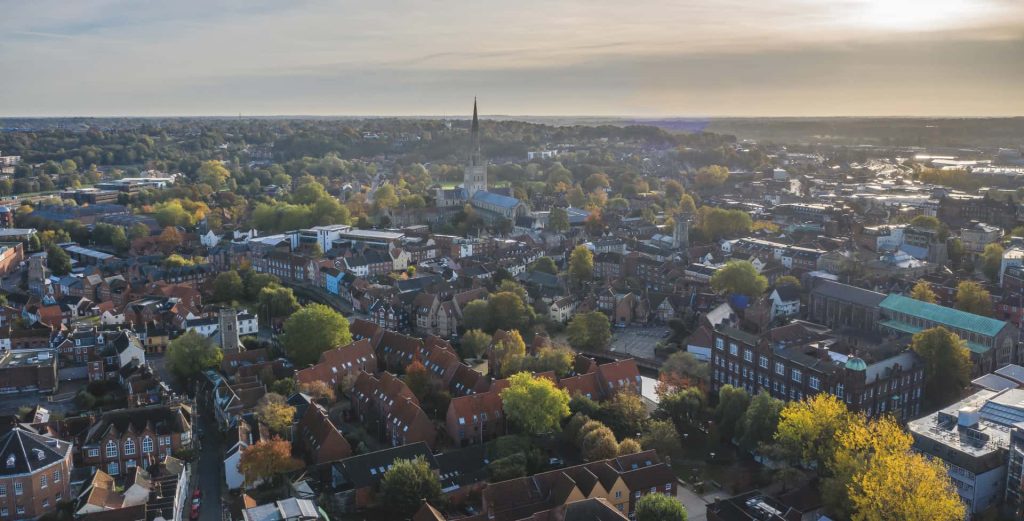 A cityscape of Norwich, overlooking trees, buildings, the Castle and the main Cathedral Spire