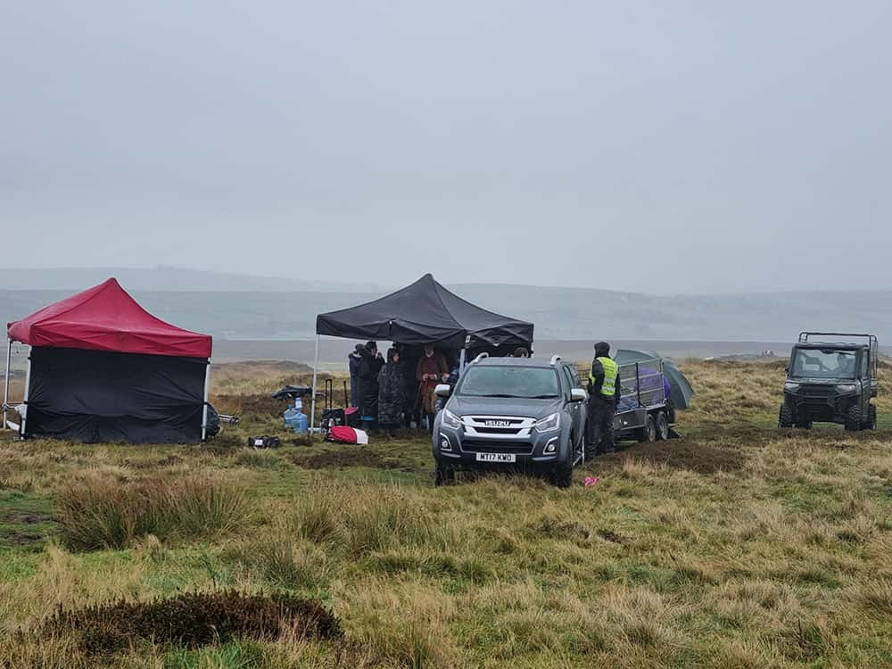 Image showing person in a high vis with a car and tents setting up a film set in a field in Yorkshire.