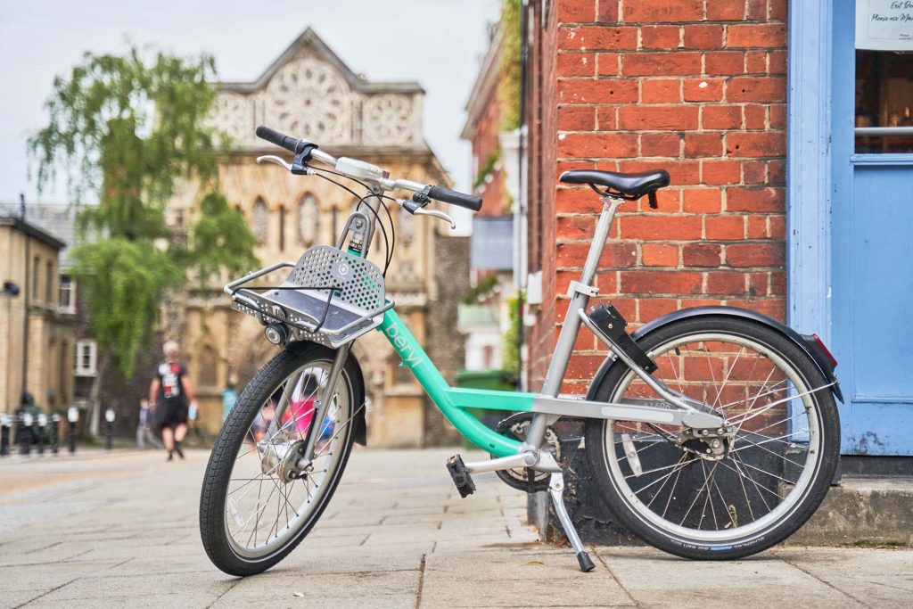 A bright teal beryl bike with a historic Norwich building in the background