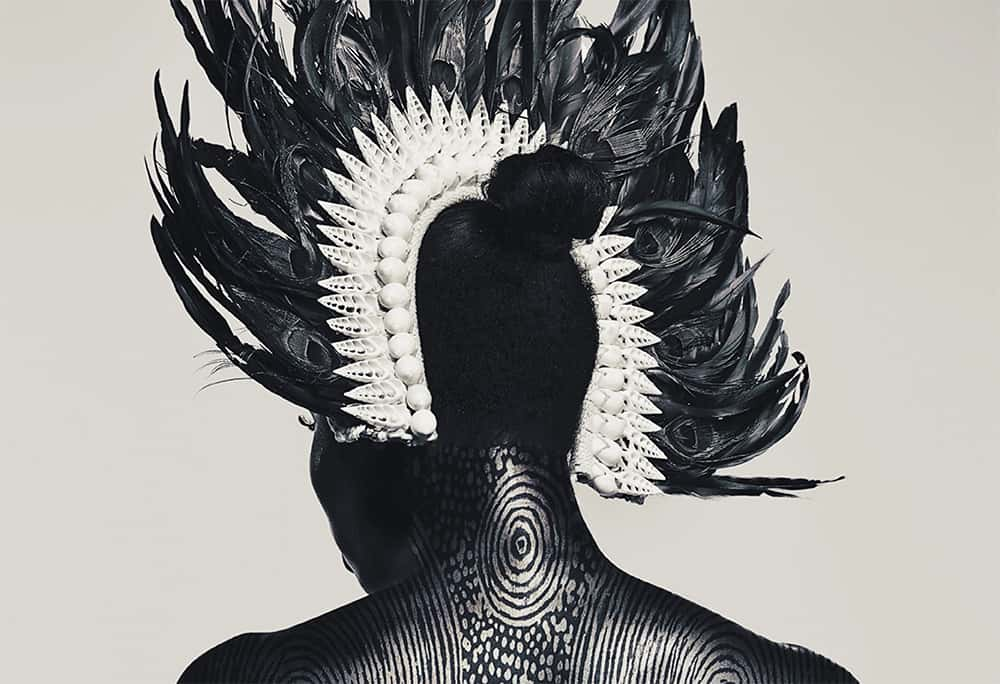 Image showing portrait of back of persons head wearing a feathered head piece. Person has hair up and has tattoos on back of neck.