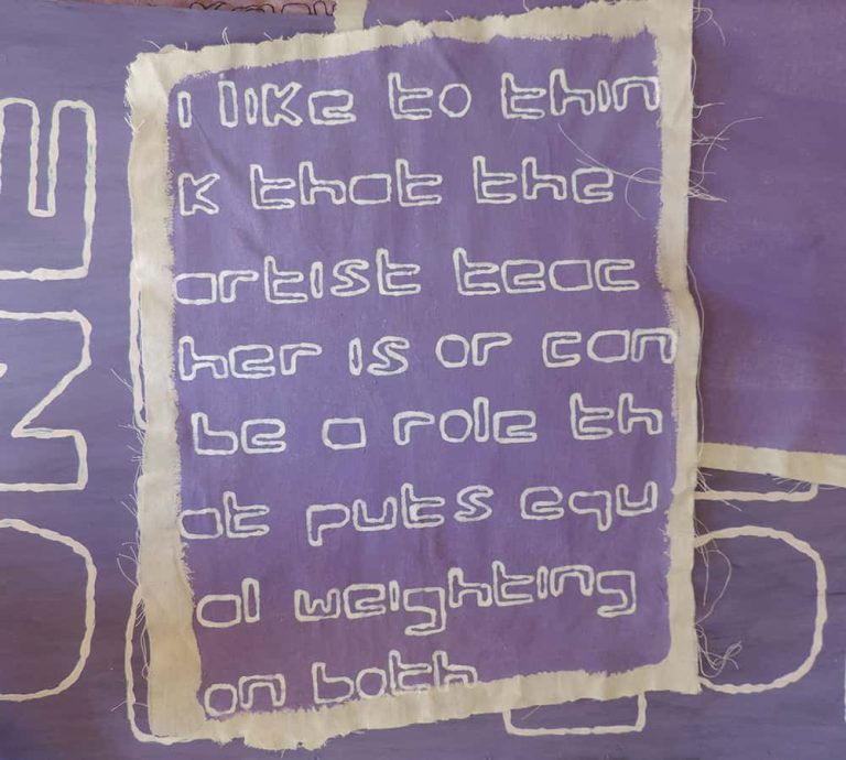 Square calico material with the words 'I like to think that the artist teacher is or can be a role that puts equal weighting on both' repeated on it overlayed on purple material