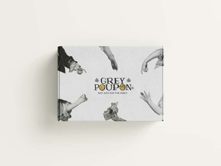 A top-down photograph of a closed pale grey gift box with Grey Poupon's branding in the centre. Around the edge of the box are cutouts of black and white photos of royalty's hands, all pointing to the logo in the centre.