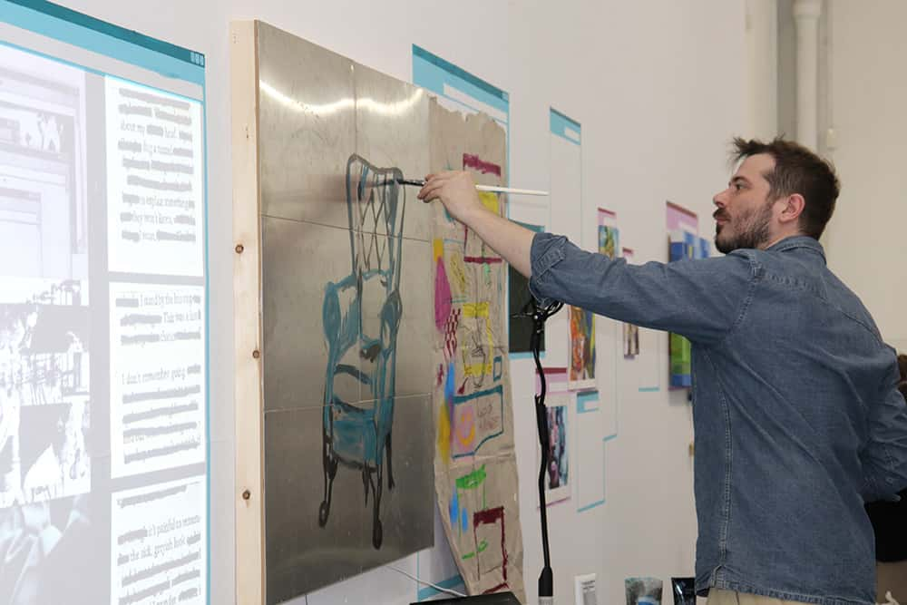 Image showing person wearing blue shirt painting on wallonto metal conductive panels with a projected screen on the left