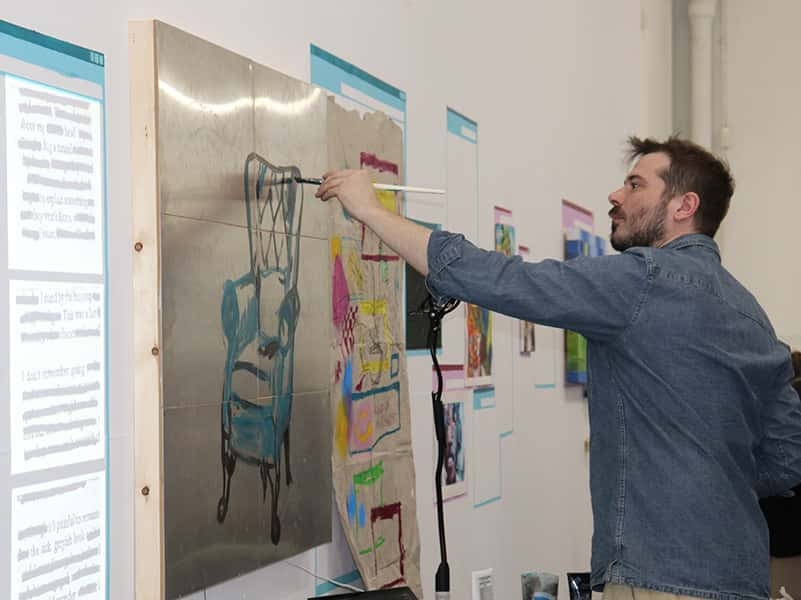 Image showing person wearing blue shirt painting on wallonto metal conductive panels with a projected screen on the left