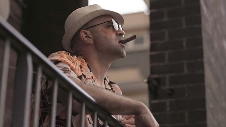 Image showing person smocking cigar on balcony wearing hat and sunglasses