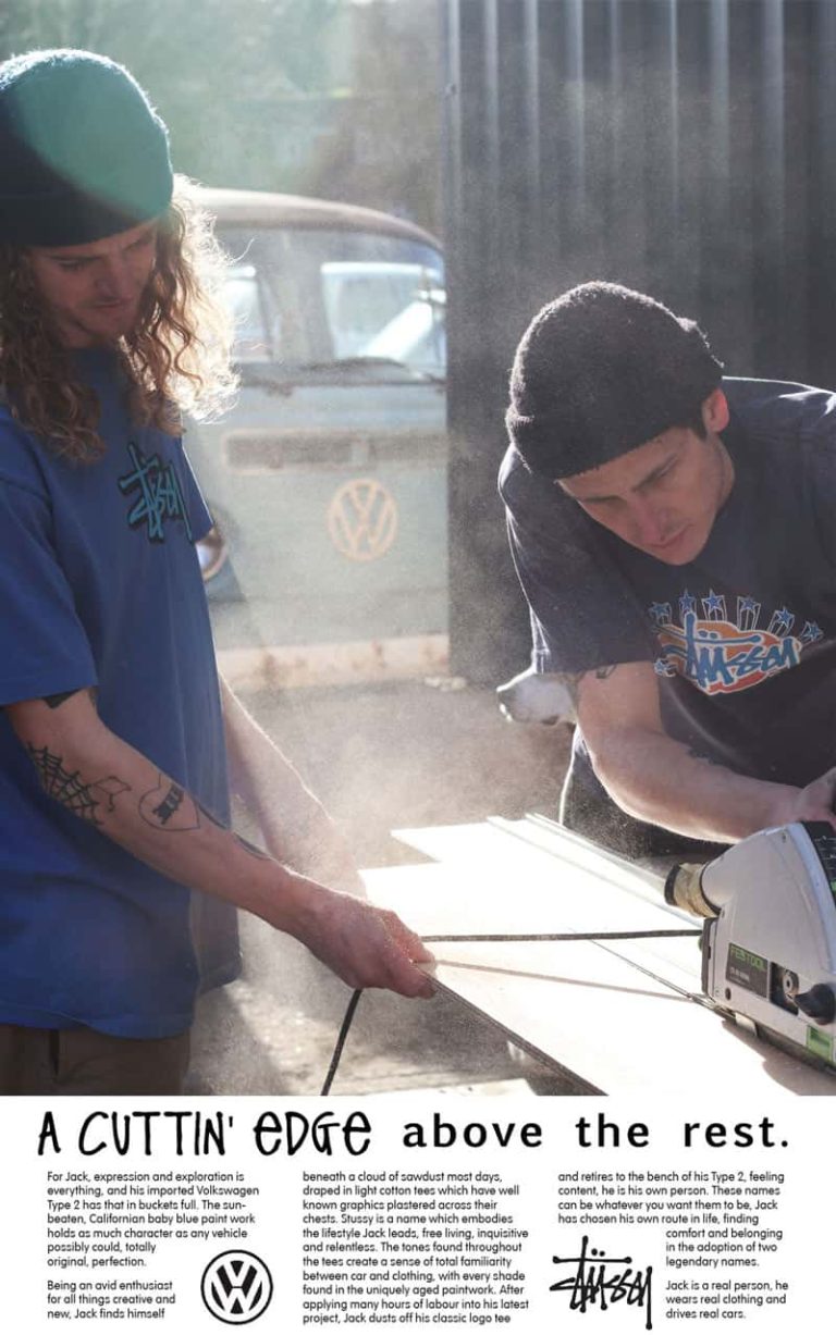 An advertising campaign poster for Stussy and Volkswagen. Two male models, wearing streetwear brand Stussy, are creating woodwork in a workshop. One model is using a circular saw, whilst the other holds a piece of wood in place. In the background is a vintage sky blue Volkswagen camper van. At the bottom of the poster is a white panel with advertising copy, with the headline 'A Cuttin' Edge Above the Rest'