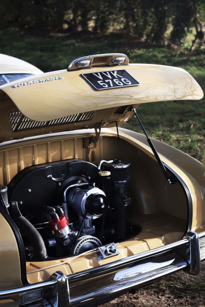 A soft-toned photograph of a classic muted yellow Volkswagen car with the boot open. Inside the boot is the exposed engine. The car is extremely clean and well cared for