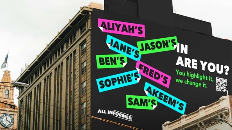 A photograph of a building, side on. On the edge of the building is a black painted wall. Placed at random angles are people's names, in a magenta, green or cyan sticker with an upturned corner. At the bottom left, the slogan 'All Informed' is in white