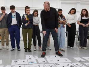 Image showing person leading workshop talking through student work on floor with students in background