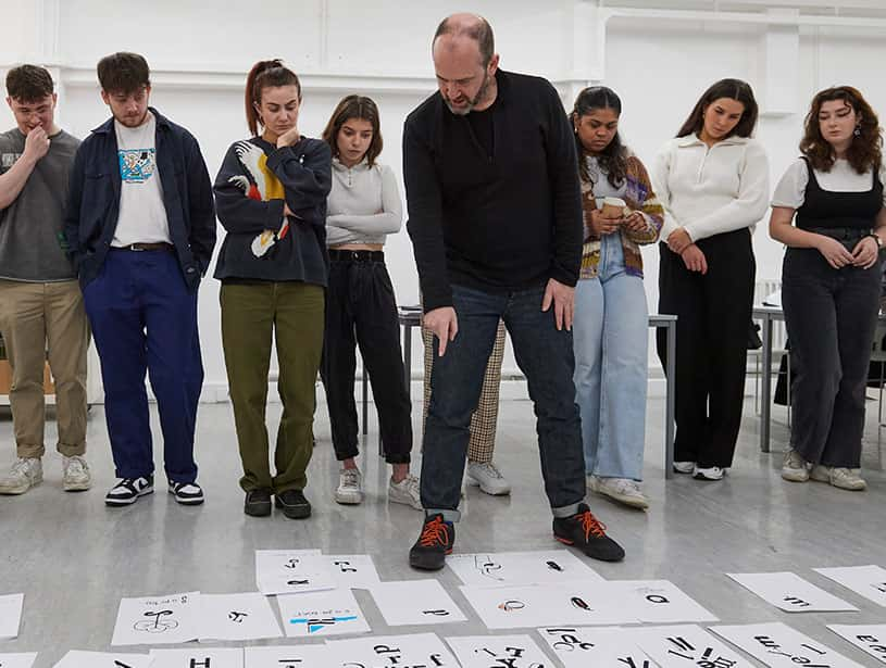 Image showing person leading workshop talking through student work on floor with students in background