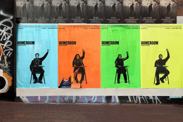 A set of four posters pasted on advertising space on a wall. Each poster is a different colour: pale blue, hot orange, neon green and highlighter yellow. The word 'Homeroom' is set to the left, in black sans serif font, written in capital letters. In the centre of each image is a black young adult sat at a single school desk, raising their hand up. The model differs per poster.