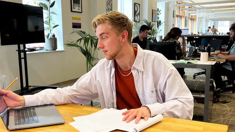 A photograph of Tim Wilcox sitting at his desk in the JKR studio, working on his laptop