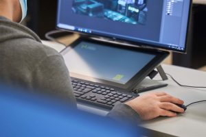 Creative technology student at Norwich University of the Arts holds a mouse next to a keyboard, tablet and a screen