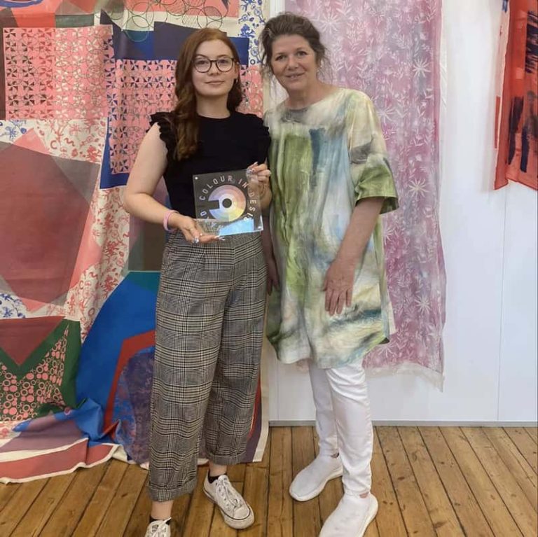 A photograph of BA Textile Design student Hollie Cooper standing next to Marianne Shillingford, Creative Director at Dulux, in the textile design studio, receiving the 'Colour in Design Award'