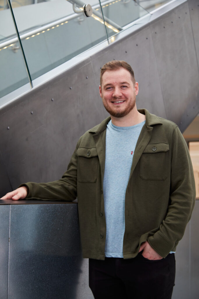 Senior Games Art and Design Lecturer Christoper Middleton Bolch portrait image. Christopher wears a thick dark green over shirt over a light blue t-shirt