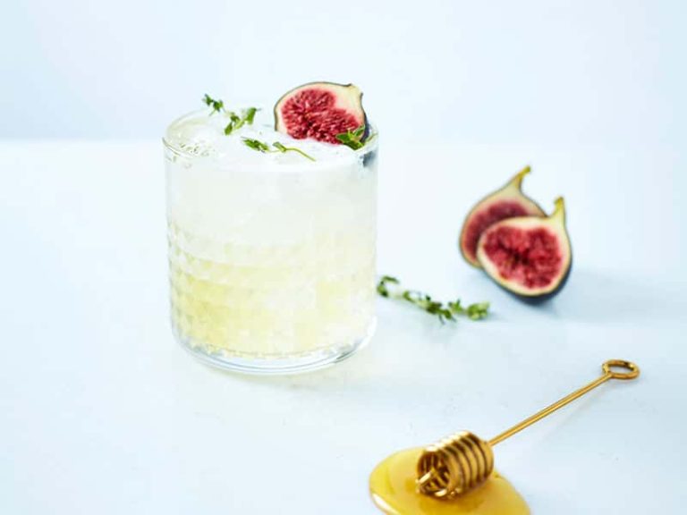 Photograph of cocktail in glass tumbler with honey stick and garnish