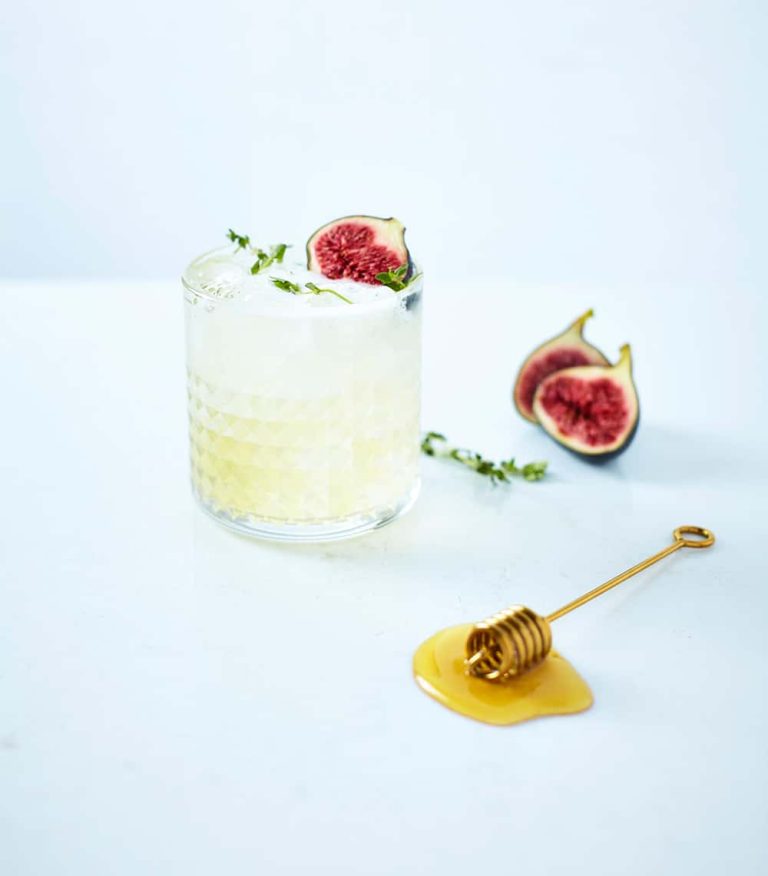 Photograph of cocktail in glass tumbler with honey stick and garnish