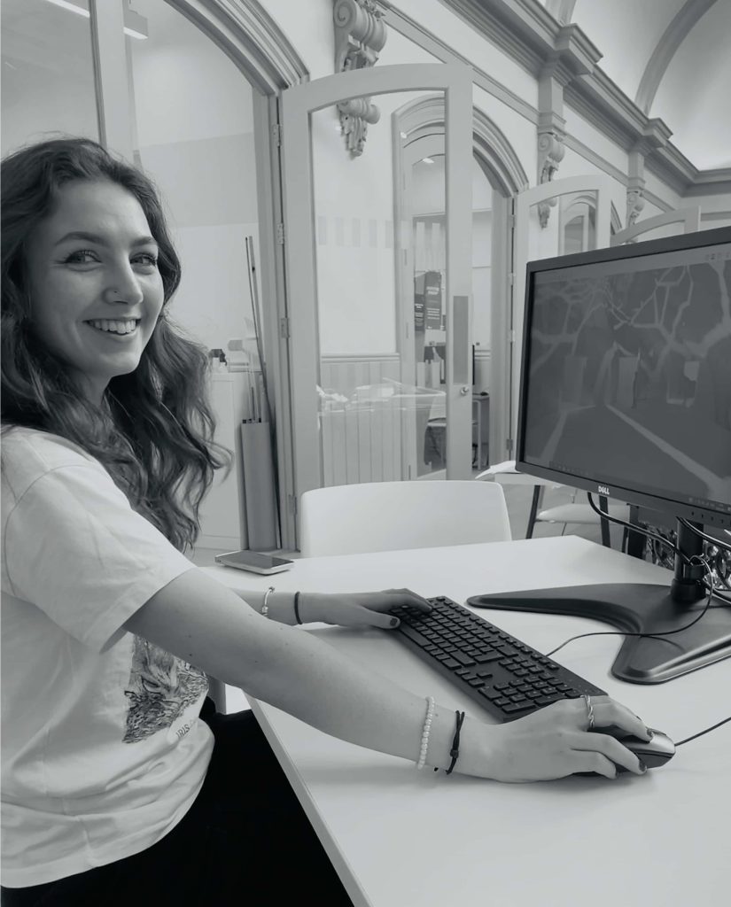 A black and white portrait of Georgia Keeble, an Interior Design student sat at a computer smiling.