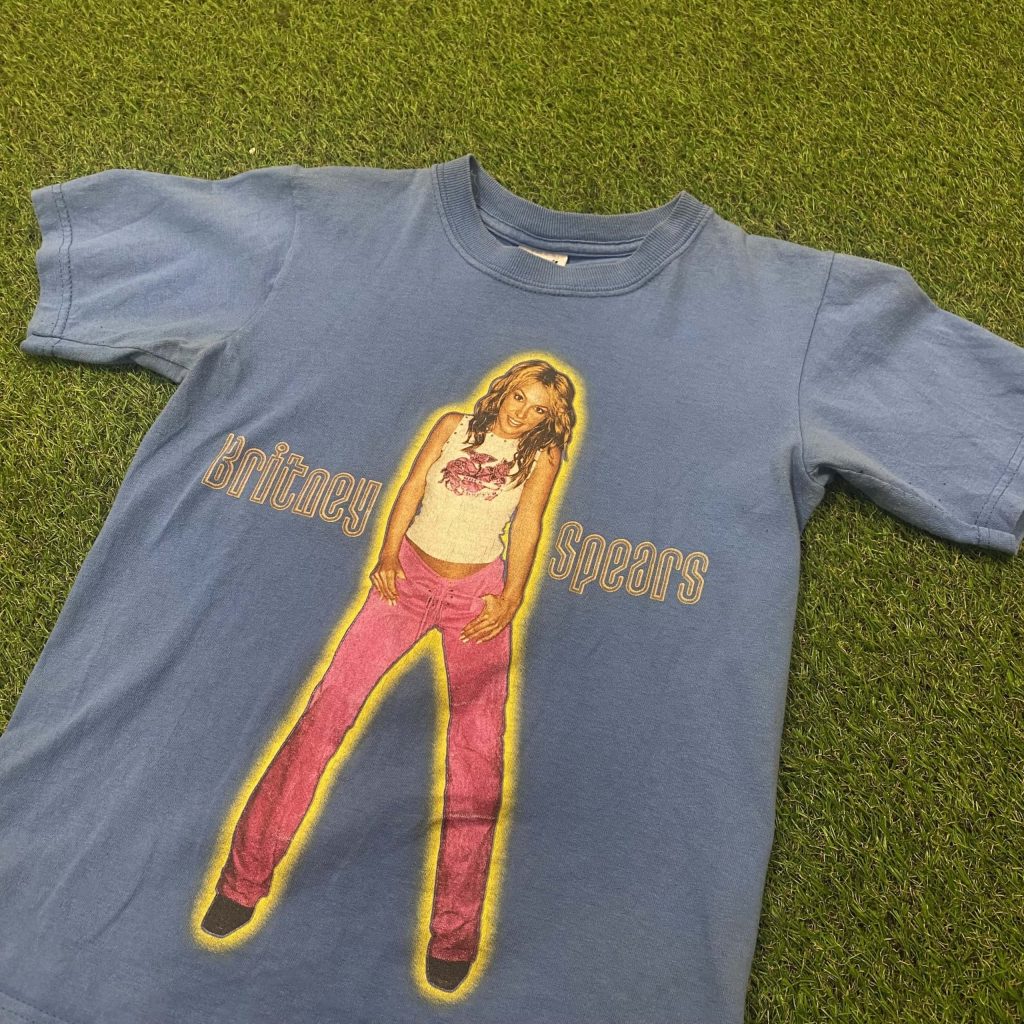 A Britney Spears blue t-shirt laid out on the floor with Britney Spears on the front with her name written on, wearing pink trousers and a white top