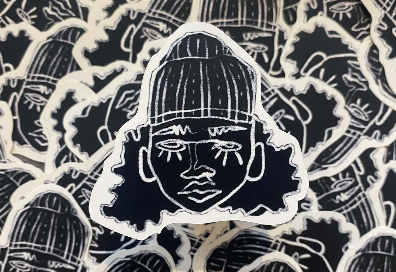 A pile of black and white stickers of the Relabelled logo, a line illustration of someone with long messy hair in a low beanie