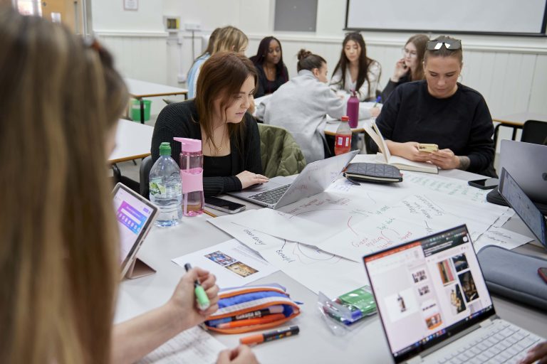 Students sitting around a table on their laptops.